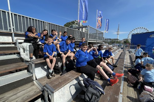 Eine Gruppe Kinder sitzen auf der Tribüne und schauen Fußball